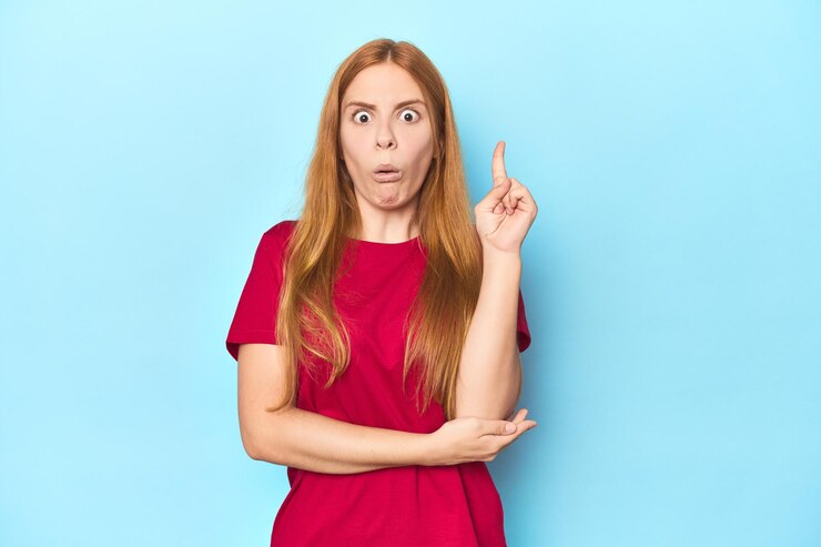 Foto mujer joven pelirroja sobre fondo azul que tiene una gran idea, concepto de creatividad