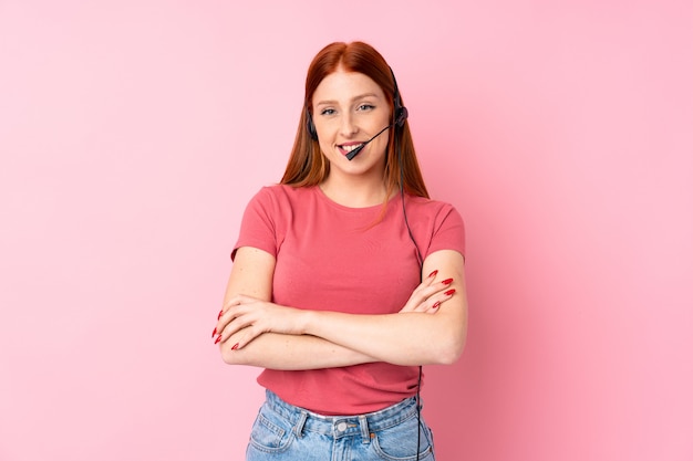 Mujer joven pelirroja sobre rosa aislado trabajando con auriculares