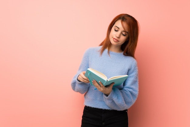 Foto mujer joven pelirroja sobre rosa sosteniendo un libro y disfrutando de la lectura