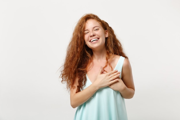 Mujer joven pelirroja sonriente divertida en ropa ligera casual posando aislada sobre fondo blanco en estudio. Concepto de estilo de vida de emociones sinceras de personas. Simulacros de espacio de copia. Manteniendo las manos en el pecho, corazón.