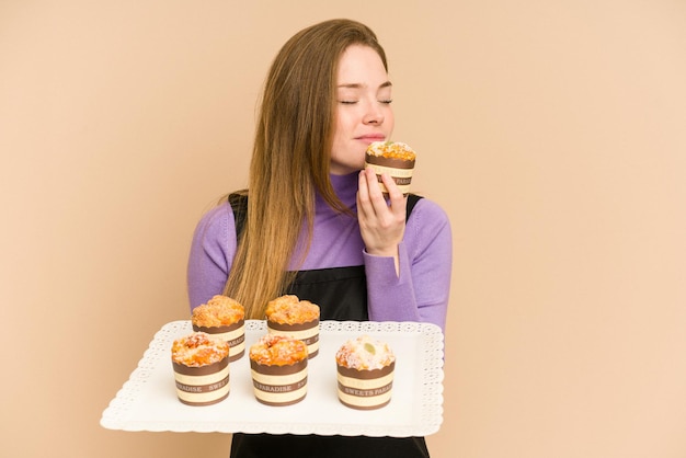 Mujer joven pelirroja sosteniendo una bandeja de muffins cortada aislada