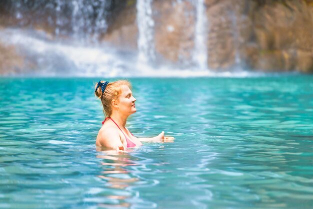 Mujer joven pelirroja en traje de baño bikini rosa se relaja en el lago tropical esmeralda con cascada Parque Nacional Erawan Kanchanaburi Tailandia