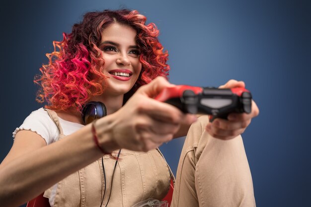 Mujer joven con pelo cyrly rojo brillante jugando videojuegos.