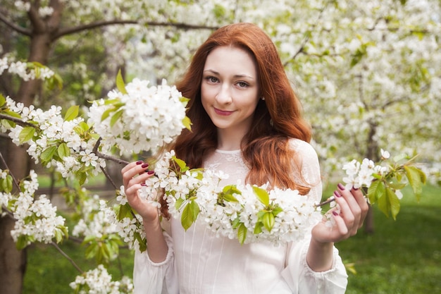 Mujer joven de pelo de jengibre cerca de un árbol floreciente tierno blanco. estado de ánimo de ensueño de hadas de la primavera y el verano. Hermosa dama romántica novia sonriente, boda. Copie el fondo del espacio.