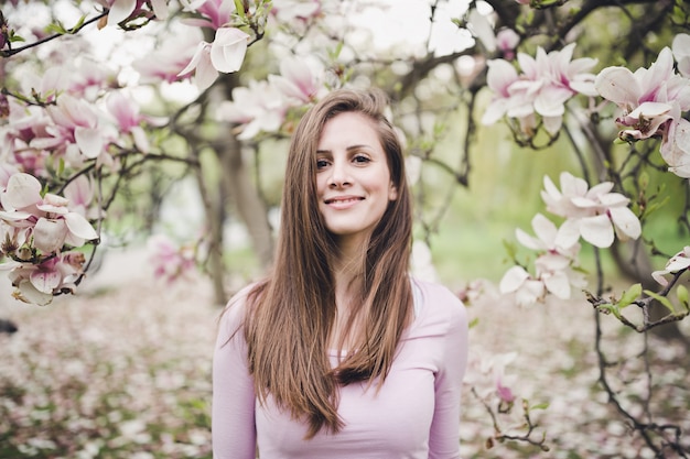 Mujer joven del pelo largo alegre bajo la magnolia floreciente.