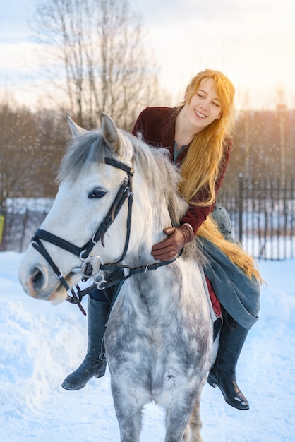 Mujer joven con pelo largo con caballo en invierno