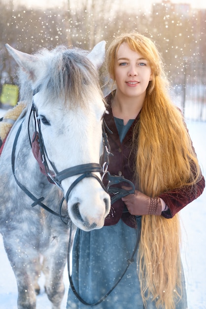 Mujer joven con pelo largo con caballo en invierno