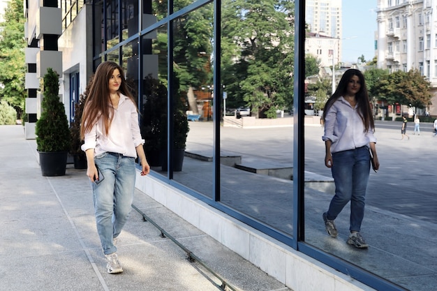 Mujer joven con pelo largo camina cerca de la pared de cristal del edificio
