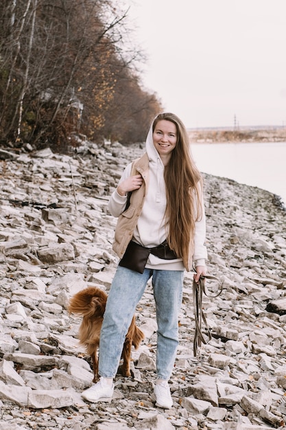 Mujer joven de pelo largo caminando con perro toller en la temporada de otoño de la orilla del río