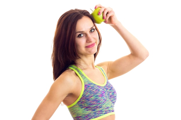 Mujer joven con el pelo largo y castaño con top deportivo de colores sosteniendo manzana verde en el estudio