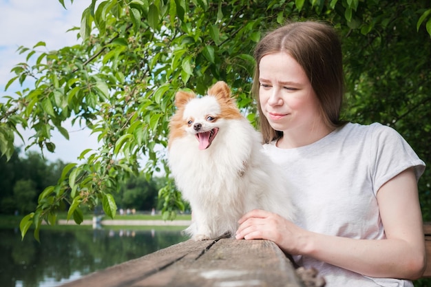 Mujer joven con el pelo largo y recto y un pequeño perro esponjoso para dar un paseo cerca del estanque de la ciudad