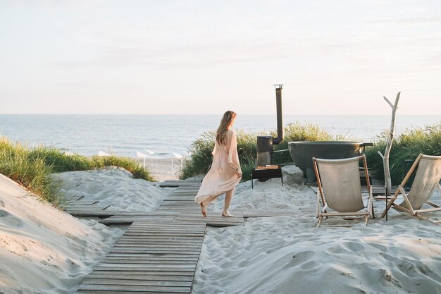 Mujer joven con el pelo largo y rubio en el centro de spa al aire libre contra el fondo del mar al atardecer