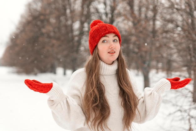 Mujer joven de pelo largo con sombrero rojo y mitones al aire libre Retrato de niña feliz caminando en el parque de invierno