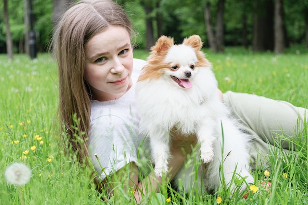 Mujer joven con el pelo largo yace en el césped del parque con un perro Pomerania