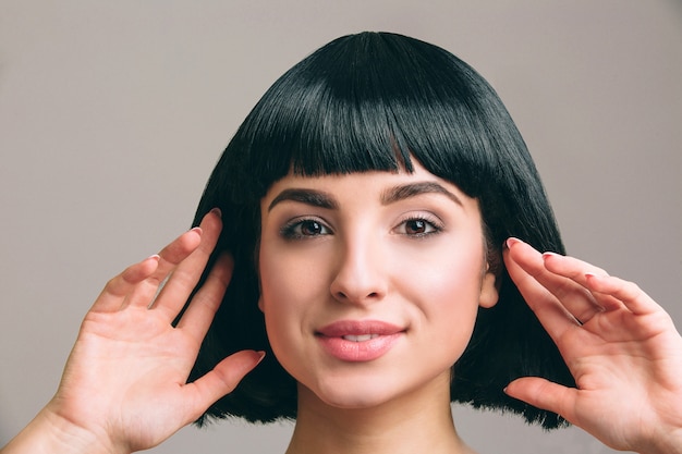 Mujer joven con pelo negro posando. Morena atractiva con corte de pelo bob. Modelo tocándolo con ambas manos.