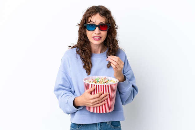 Mujer joven con pelo rizado aislado sobre fondo blanco con gafas 3d y sosteniendo un gran balde de palomitas de maíz