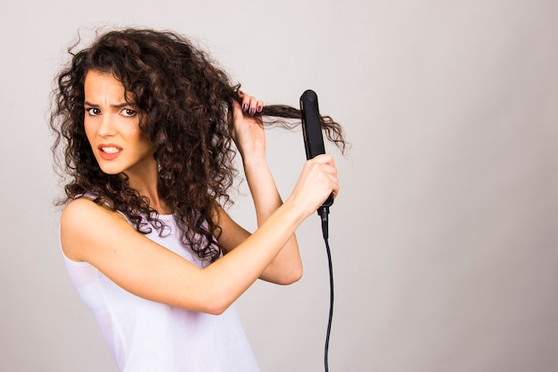 Mujer joven con pelo rizado con plancha de pelo