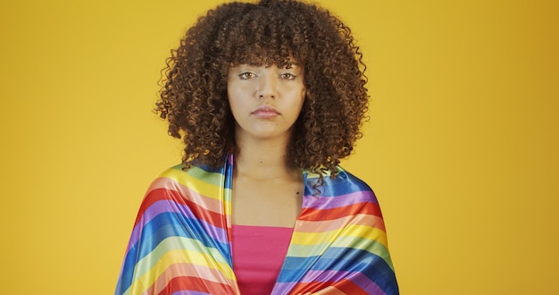 Mujer joven de pelo rizado que cubre con la bandera del orgullo lgbt manteniendo el puño en alto cubriendo la bandera lgbt