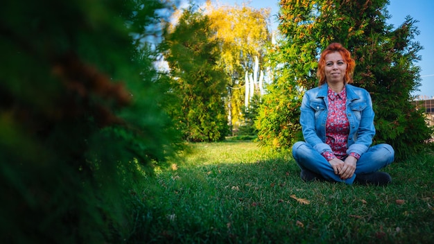 Mujer joven con el pelo rojo entre los árboles Retrato de mujer joven atractiva con peinado de moda de pie en el jardín de primavera y mirando a la cámara