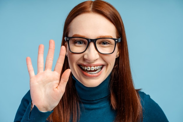 Mujer joven de pelo rojo con gafas y aparatos ortopédicos saluda su sonrisa iluminando la foto