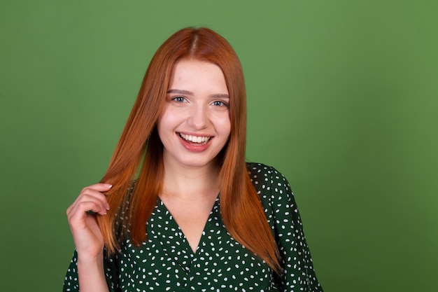 Mujer joven de pelo rojo en la pared verde sonríe y ríe, de buen humor, emociones positivas