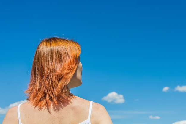 Mujer joven de pelo rojo se ve en el concepto de espacio de copia de viajes de belleza de cielo azul