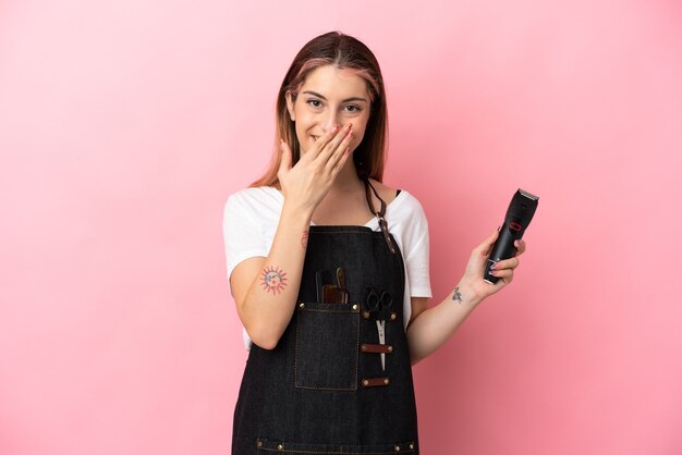 Mujer joven peluquera aislada en rosa feliz y sonriente cubriendo la boca con la mano