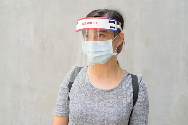 Mujer joven pensando con máscara y protector facial para protegerse del brote de virus corona al aire libre