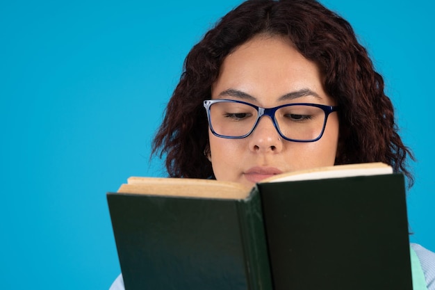 Mujer joven pensativa con gafas leyendo un libro de tapa dura