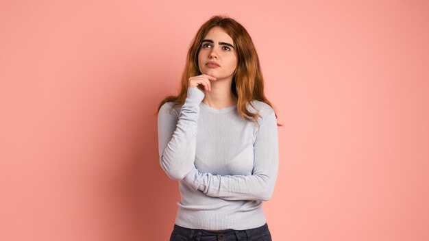 Mujer joven pensativa mirando hacia arriba en el estudio rosa