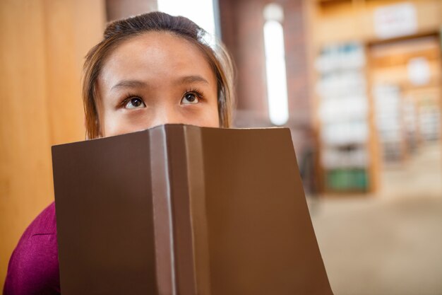 Mujer joven pensativa que cubre su rostro con el libro