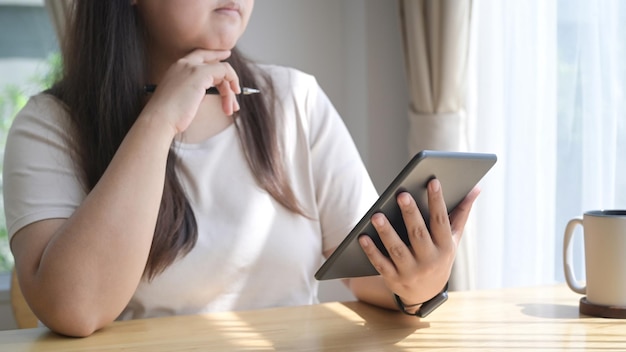 Mujer joven pensativa usando tableta digital navegando por internet en casa