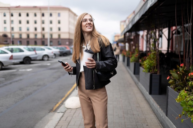 Mujer joven periodista camina por la ciudad con café en las manos