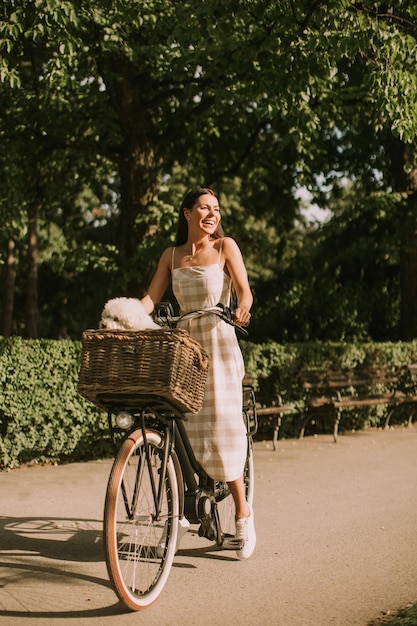 Mujer joven con perro bichon frise blanco en la cesta de la bicicleta eléctrica