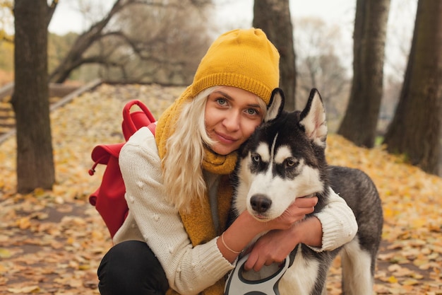 Mujer joven con perro husky caricias en el parque de otoño