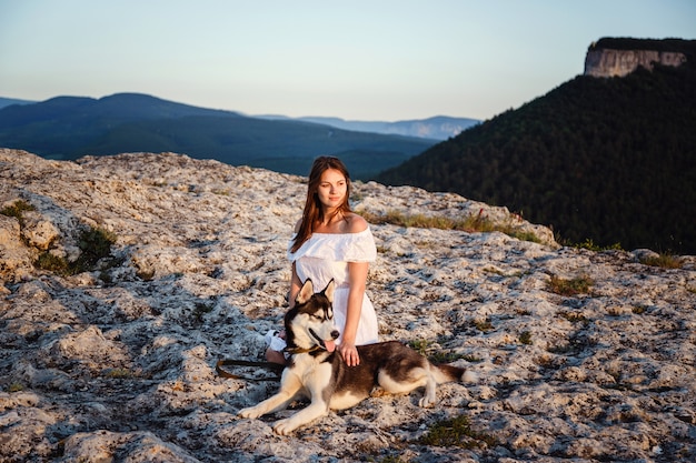 Mujer joven con perro Husky en un día soleado sentado en alta montaña