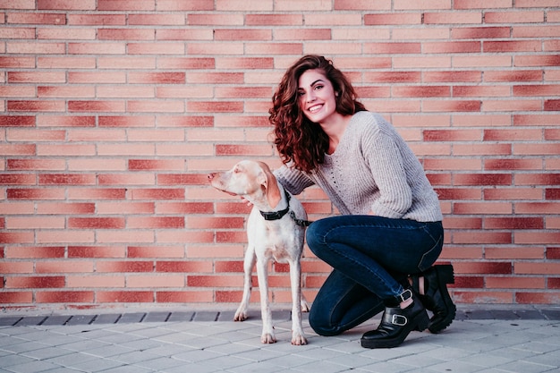 Foto mujer joven con perro en la pared de ladrillo