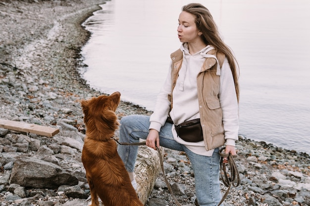 Mujer joven y perro perdiguero camina en la orilla del río en la temporada de otoño