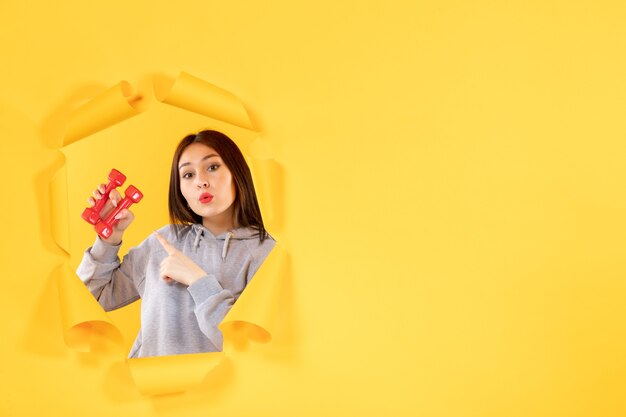 Mujer joven con pesas sobre fondo amarillo atleta de ejercicio de gimnasio