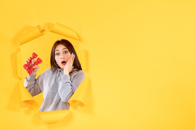 Mujer joven con pesas sobre fondo amarillo ejercicio ajuste atleta