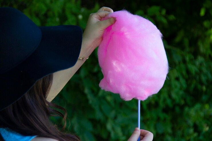 Foto mujer joven de pie con algodón de azúcar rosa al aire libre