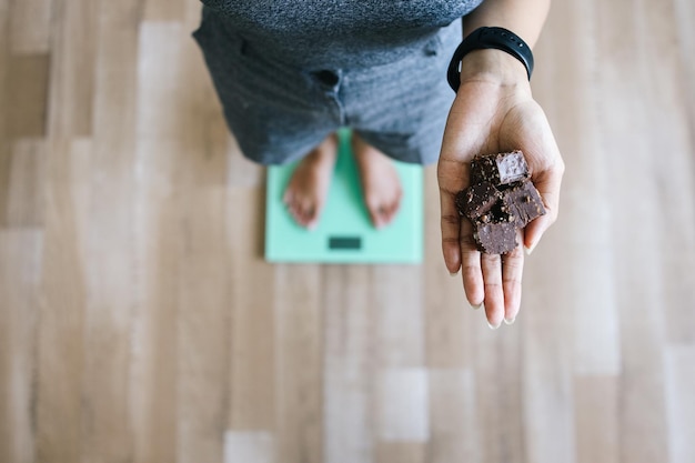 Mujer joven de pie en la balanza y sosteniendo una barra de chocolate