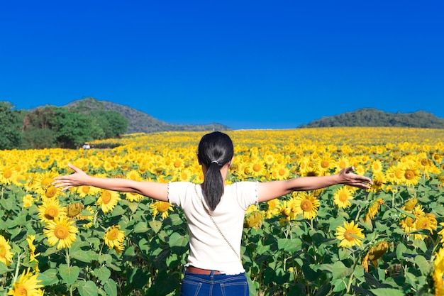 Mujer joven de pie con los brazos extendidos en el campo de girasoles de colores brillantes al sol del mediodía en una ladera