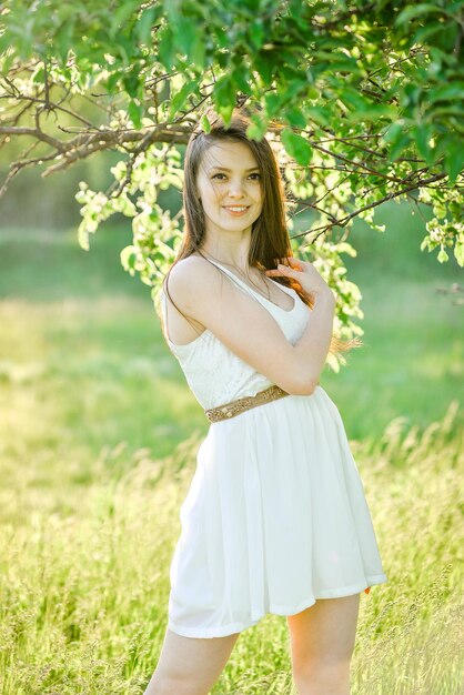 Foto una mujer joven está de pie en un campo con un árbol en el fondo