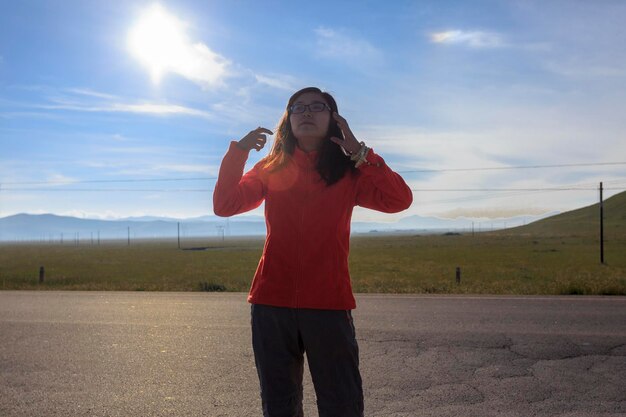 Foto mujer joven de pie en la carretera por el paisaje durante un día soleado