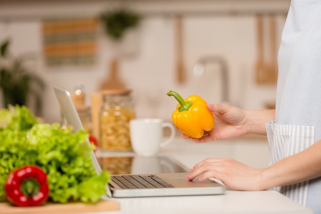 Mujer joven de pie en la cocina con el portátil y mirando recetas. Concepto de comida. De cerca.