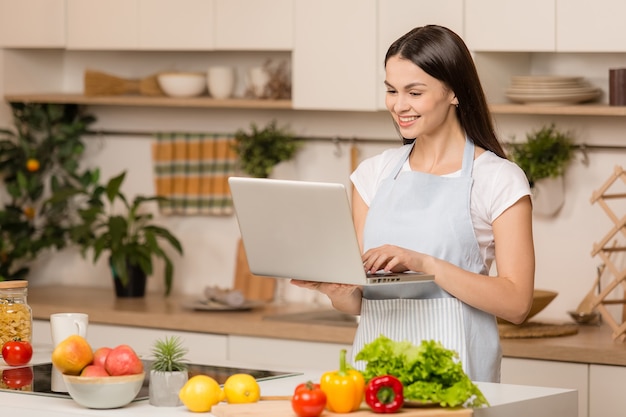 Mujer joven de pie en la cocina con portátil