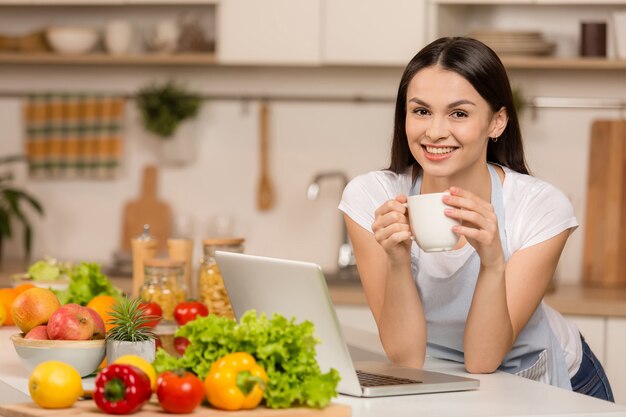 Mujer joven de pie en la cocina con portátil