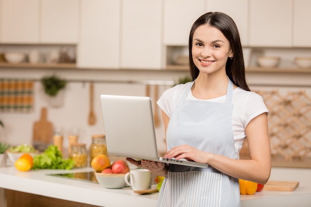 Mujer joven de pie en la cocina con portátil