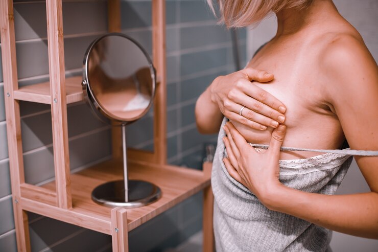 Mujer joven de pie frente al espejo, comprobando su pecho mientras se autoexamina. Conciencia del cáncer de mama. ¿Cómo verifico el concepto de mama?